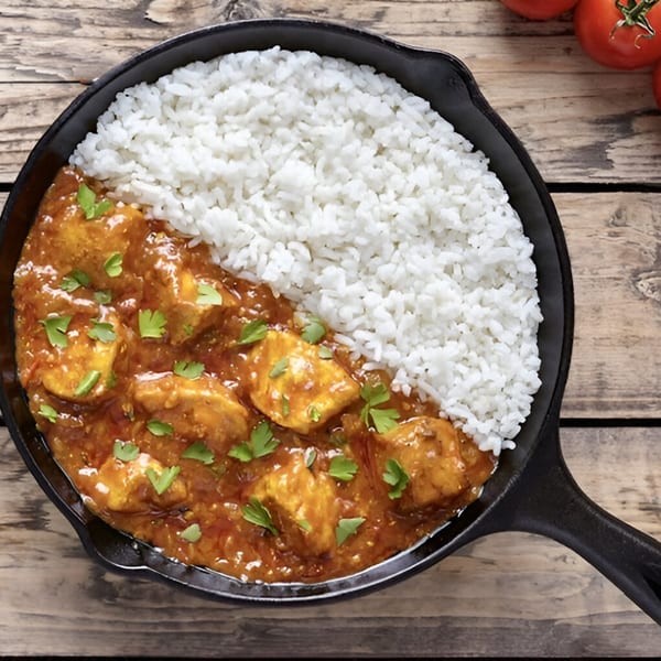 Indian chicken curry with rice, garnished with cilantro, served in a black skillet on a wooden table.