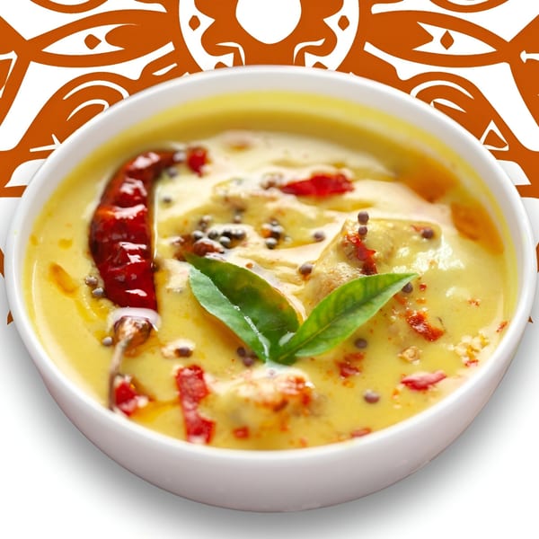 Creamy yellow Indian curry with red chilies, mustard seeds, and green leaves in a white bowl.