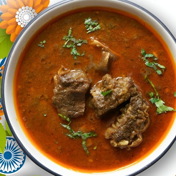 A bowl of rich, red Indian curry with tender meat pieces and fresh cilantro garnish.